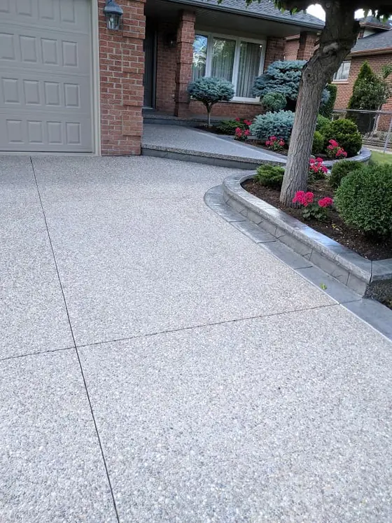 Exposed aggregate driveway and entrance bordered by garden beds