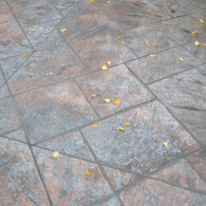 Terracotta stamped concrete before sealing, with a faded, chalky surface and scattered leaves